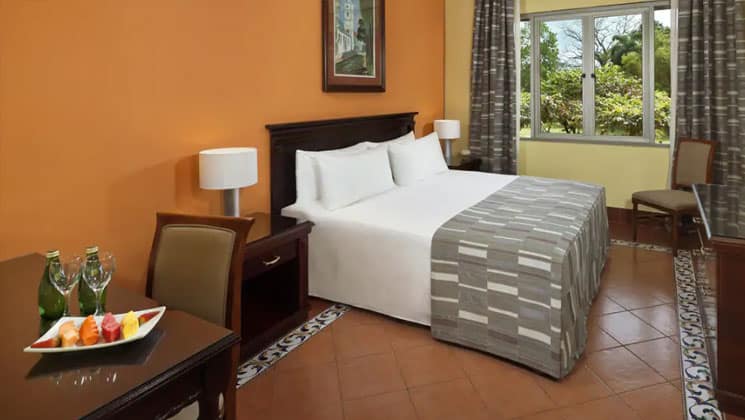 room with a large white bed with grey checked blanked on it, yellow wall and window at melia hotel panama canal