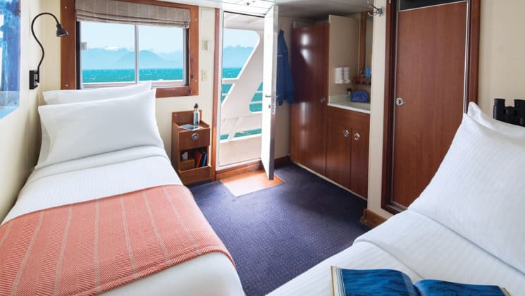 National Geographic Sea Lion Category 2 stateroom with 2 twin beds, closet, bathroom, picture window, and door that opens to deck.