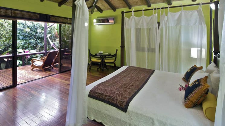 The deluxe room with a queen-sized bed, yellow walls, white linens, and a private patio at the Nayara Hotel, Spa & Gardens, a luxury boutique hotel in Costa Rica