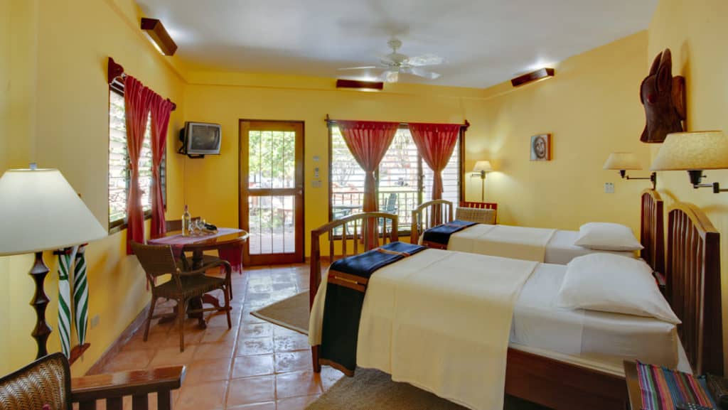 A room with yellow walls, window views, and two double beds at the Inn at Robert's Grove, a boutique hotel ideal after a day exploring Belize's barrier reef or tropical rainforest