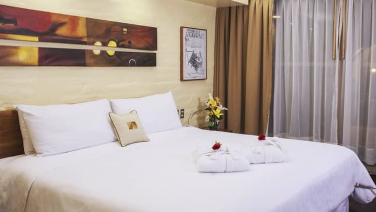 A room with a king-sized bed, white sheets, artwork, and drapes at Sonesta Posada Del Inca Arequipa, a luxury boutique hotel