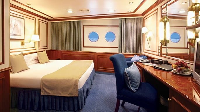 Solo cabin with portholes, blue carpet and chairs with sage green window shades aboard national geographic Orion