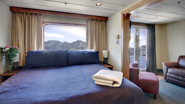 Commodore suite aboard the safari endeavour Alaska small ship, with a large blue bed, adjoining room, and large windows