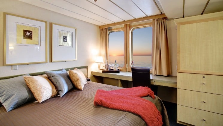 Safari endeavour Alaska small ship admiral cabin with a large bed, two large windows looking at the ocean, and desk