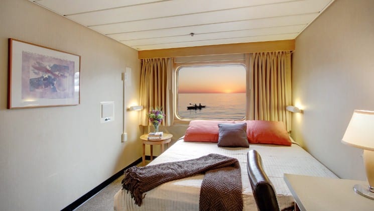 Pathfinder cabin aboard the safari endeavour Baja small ship, with large bed, lamp, and window looking out at the sunset