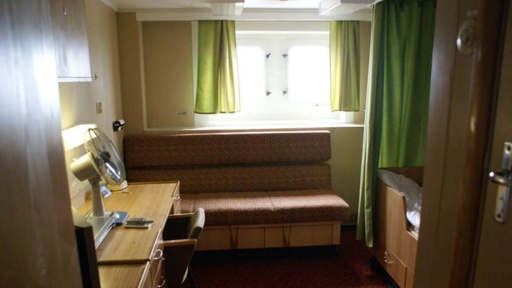 Bench seating with desk, fan, chair twin berth, bathroom and window.