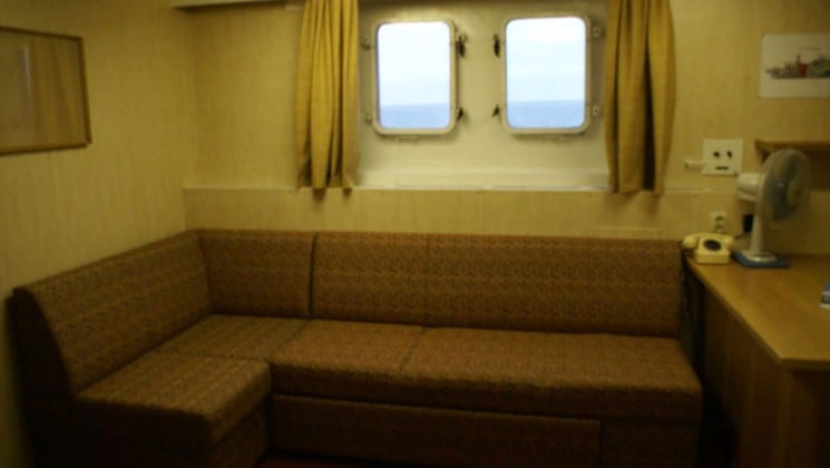 Banquette seating with desk and 2 large portholes in the Victory Suite aboard the 50 Years of Victory.