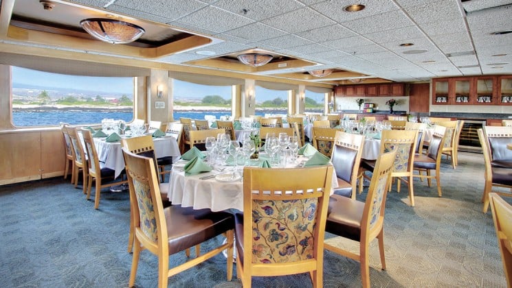 Dining area with a large tables surrounded by chairs and large windows aboard the safari endeavour small Alaska ship