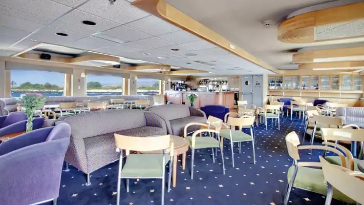 Dining room aboard the safari endeavour baja small ship with rows of chairs and couches and windows