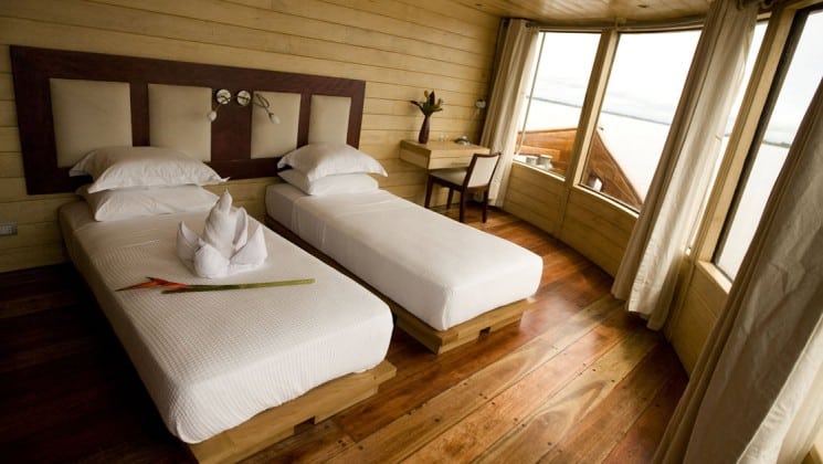 Master Suite with two twin beds, desk, chair and large picture windows aboard Delfin II riverboat on Amazon River cruise