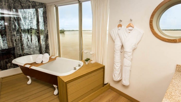 Bathroom with shower, tub, large window and porthole in Master Suite aboard Delfin III riverboat on Amazon River cruise