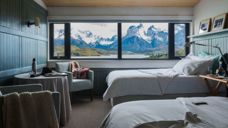 Two beds, a small table and two chairs in the Cordillera Paine Room at Explora Torres del Paine Lodge in Chile, with lake and mountain views