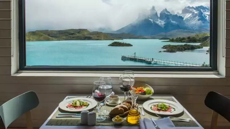 Lunch served with wine at a table for two at large window with lake and mountain views at Explora Patagonia Torres del Paine Lodge in Chile