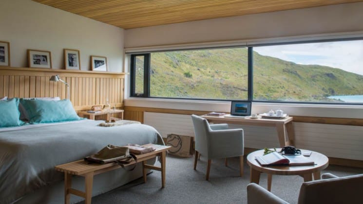Large bed, writing desk, small table and two chairs in Exploradores Suite looking out to Lake Pehoe at Explora Torres del Paine Lodge in Chile