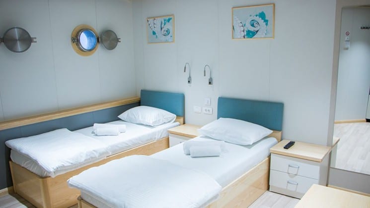 Fantazija stateroom with 2 twin beds, nightstand, seating with portholes.
