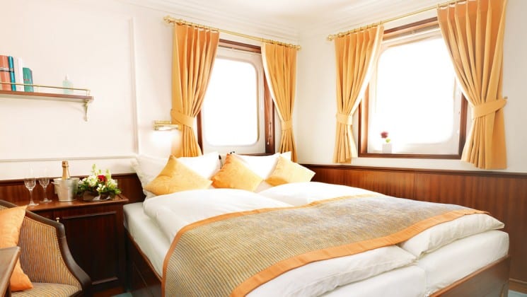 cabin with large bed, 2 large windows, a table and chair on the Lindblad Sea Cloud mediterranean luxury yacht