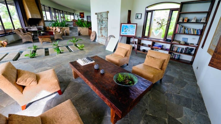 Lodge interior with coffee tables, chairs, book cases and plants at Galapagos Safari Camp Santa Cruz Highlands in the Galapagos Islands
