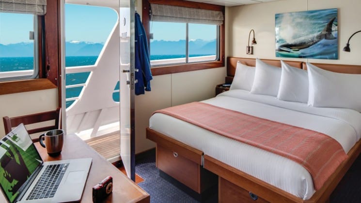 Large bed, desk, chair, large windows and door opening to outside aboard National Geographic Sea Bird expedition ship