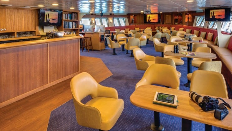 Tables and chairs near bar in window-lined lounge aboard National Geographic Sea Bird expedition ship