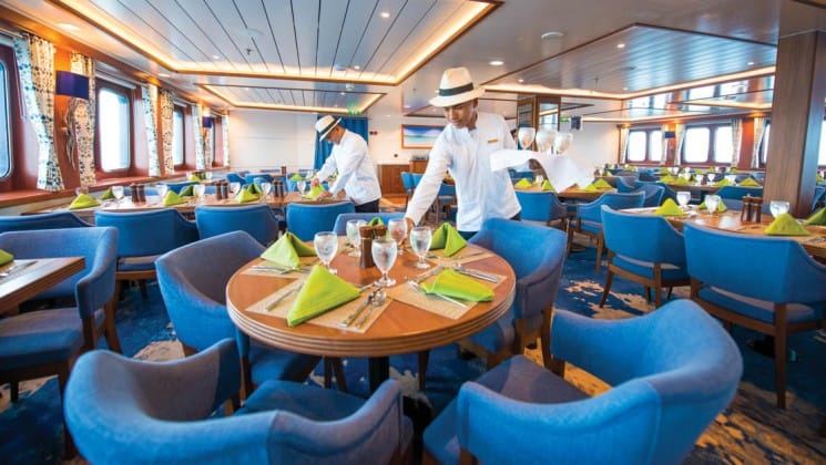 Crew members set the tables in the dining room awash with natural light aboard National Geographic Endeavour II expedition ship in the Galapagos Islands