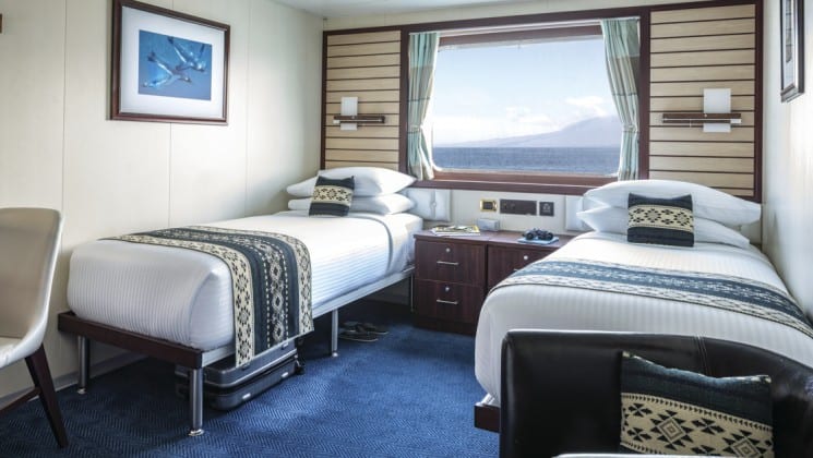 Two beds, bedside table, two chairs and large window in Category 4 cabin aboard National Geographic Endeavour II expedition ship in the Galapagos Islands