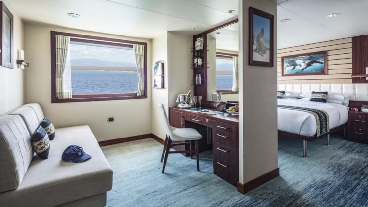 Suite C interior with large bed, couch, desk, chair and large windows aboard National Geographic Endeavour II expedition ship in the Galapagos Islands