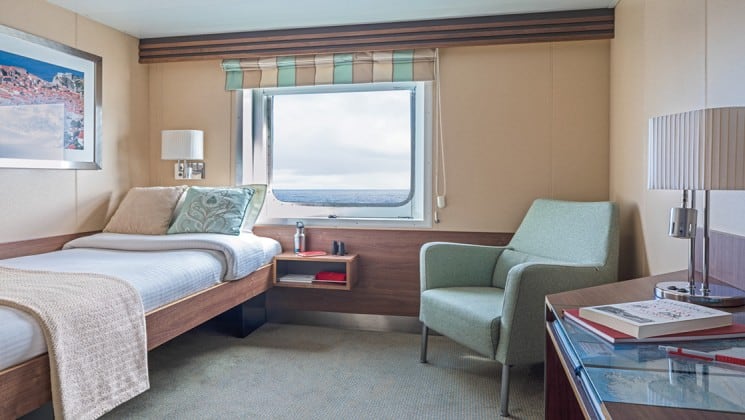 Category A Solo cabin with bed, nightstand, desk, chair and large window aboard National Geographic Explorer polar expedition ship