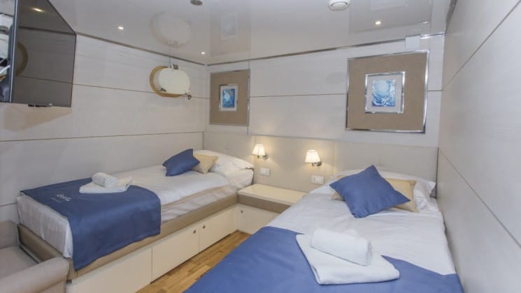 Riva Croatia small ship lower deck cabin with 2 beds, pictures on the wall, a porthole and blue and wood accents