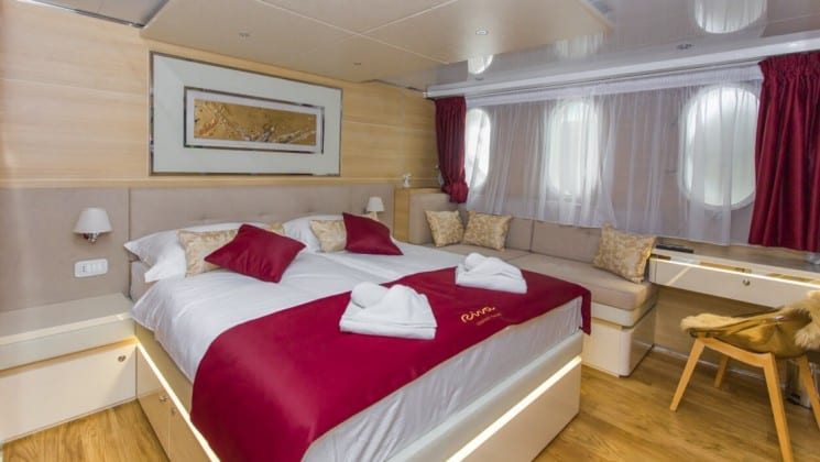 Riva Croatia small ship main deck cabin with large bed, wood accents and window with a curtain behind it