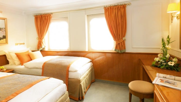 cabin with 2 beds, 2 large windows, a desk and a stool aboard the Lindblad sea cloud mediterranean luxury small ship