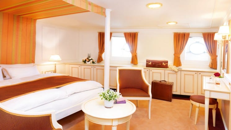 category c cabin with a large bed, table and chairs aboard the Lindblad Sea Cloud luxury mediterranean yacht