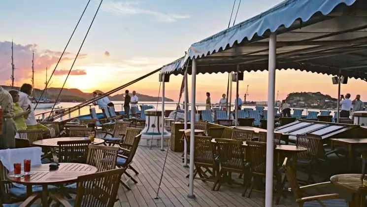 rows of tables and chairs lining the deck of the sea cloud ii mediterranean luxury small ship at sunset, with a covered bar on the right