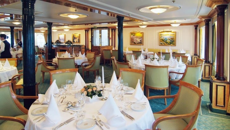 dining area with white tables, green chairs and pictures on the walls aboard the sea cloud ii mediterranean luxury yacht