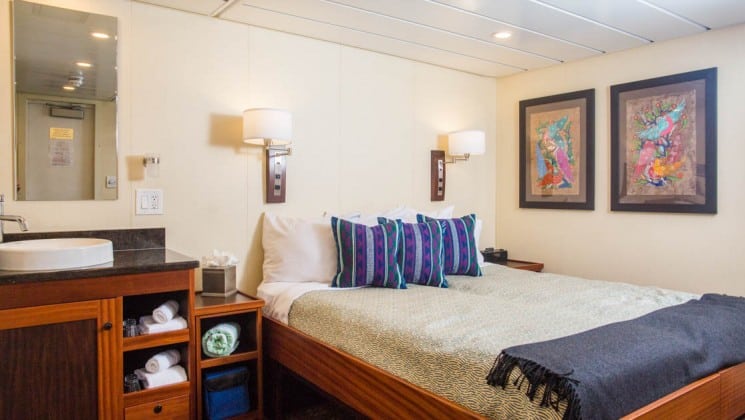 Safari Voyager Costa Rica small ship admiral cabin with a queen bed, pictures and lights on the walls and a desk next to the bed