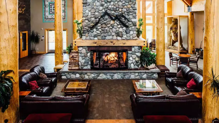 Spacious lobby with river rock fire place with several leather couches surrounding it at Talkeetna Lodge in Alaska.