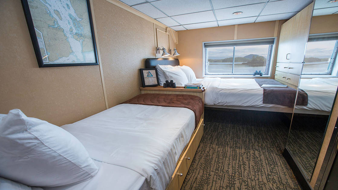 Category A stateroom aboard Baranof Dream with two single beds, window, and mirror.
