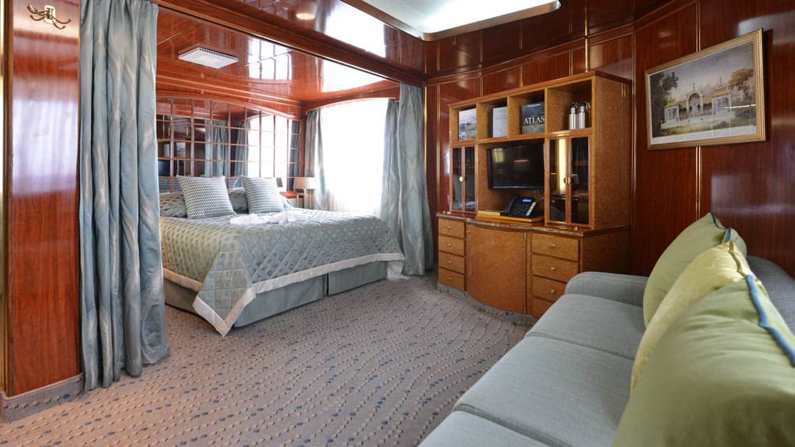 Hebridean Sky Deluxe suite with large picture windows, queen bed, couch and chair, nightstands and dresser.
