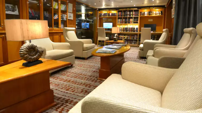 Library and sitting room with books, chairs and tables on board the Hebridean Sky