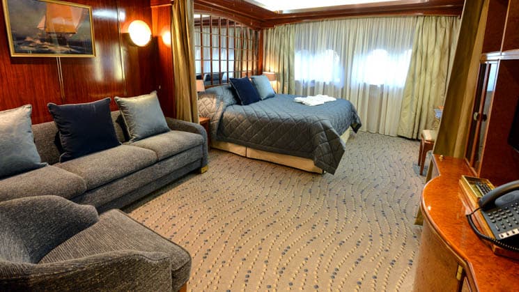 Single Suite aboard Hebridean Sky 21 polar expedition ship, with two twin beds pushed together into a double, two portholes, couch & chair, all in dark blue linens with light tan accents.