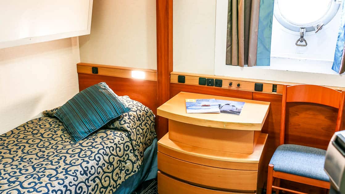 ocean endeavour ship cabin with a bed, nightstand, porthole and chair