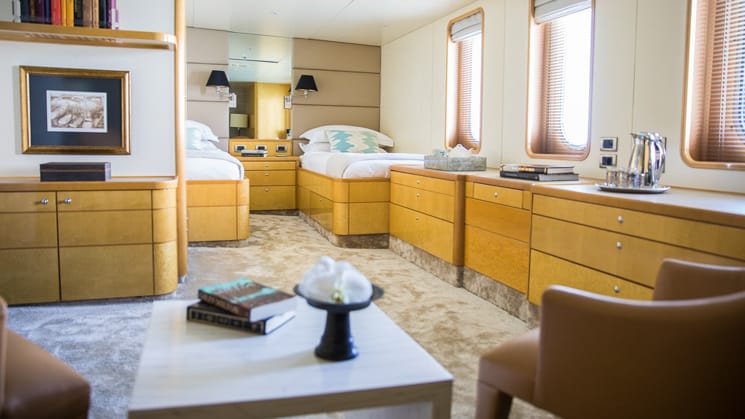 two twin beds with vertical windows, mostly wooden accents and furniture with small seating area, bookshelf, a category 3 cabin board Indonesia yacht aqua blu