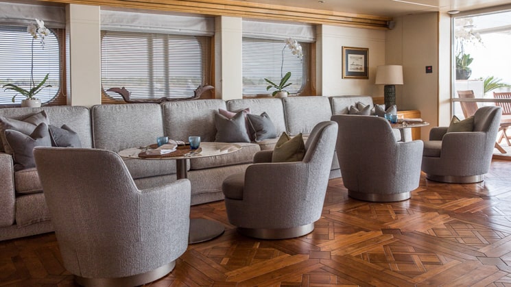Lounge area aboard Indonesia yacht Aqua Blu wooden flooring below grey blue arm chairs and couches