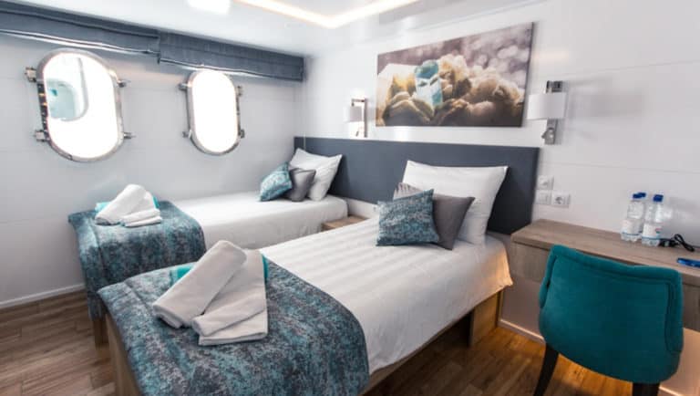 Lower Deck cabin aboard Aquamarin Croatia yacht with 2 twin beds, 2 portholes, desk & chair, with turquoise, silver & white accents throughout.