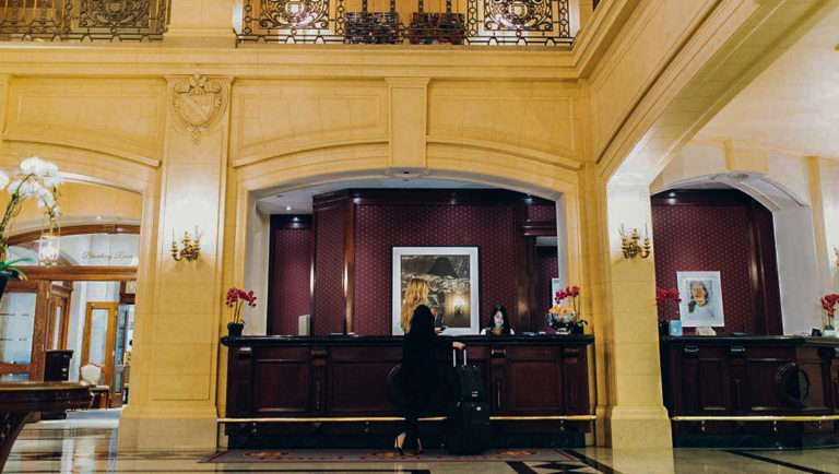 Reception area at Fort Garry Hotel in Churchill, Canada, with a large, castle-like feel, orchids & blonde woman with luggage standing at the mahogany desk.