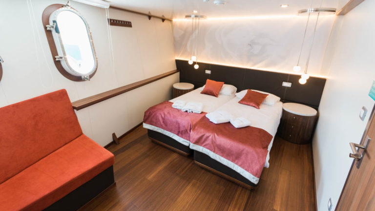 Lower Deck Cabin with porthole, couch, and bed aboard Avangard.