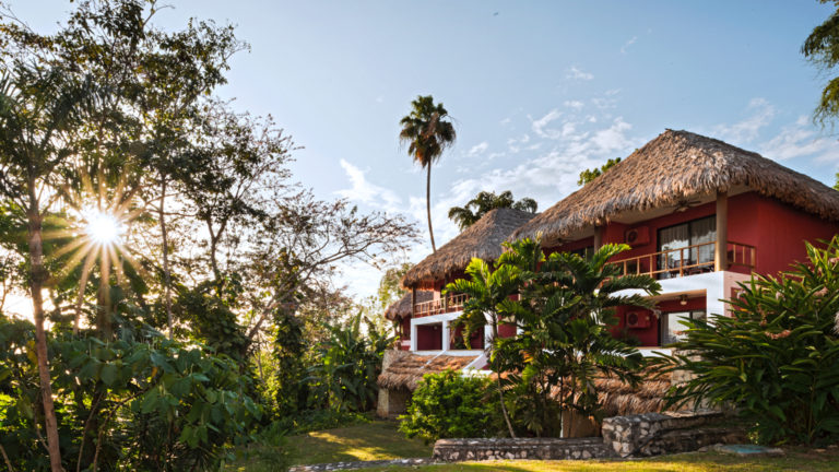 Exterior view of Camino Real Tikal Hotel in Guatemala with sun shining through the palm trees and clear blue skies