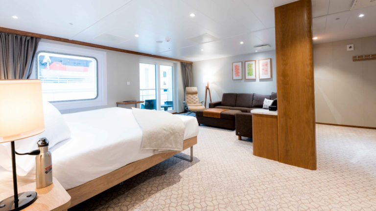 Bridge Deck Suite aboard Coral Adventurer with large bed, lounge area, and entry way.