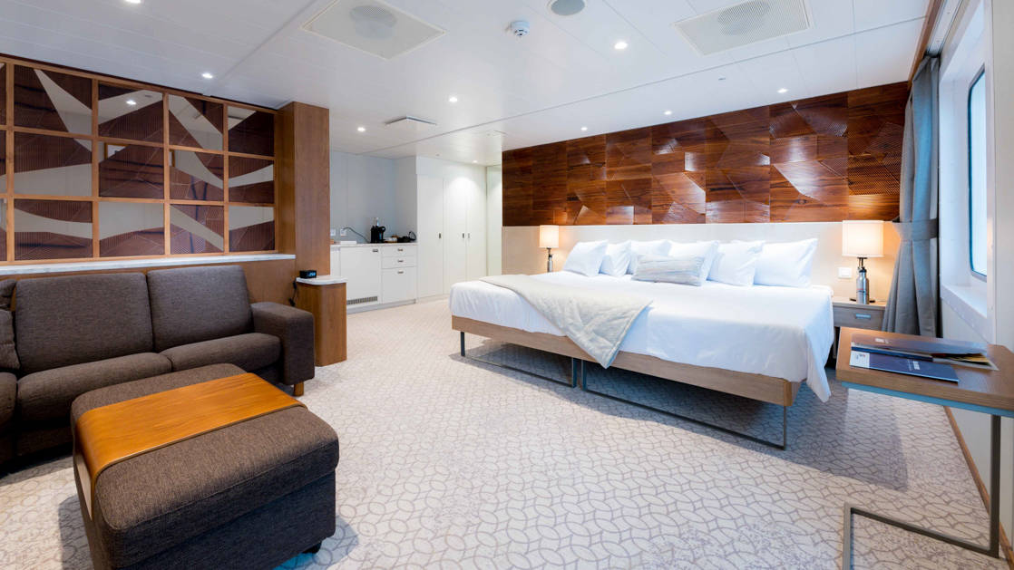 Bridge Deck Suite aboard Coral Geographer with large bed, sitting area, and entry way.