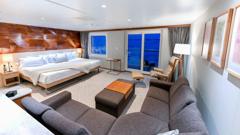 Bridge Deck Suite aboard Coral Adventurer with large bed, verandah, and sectional couch.