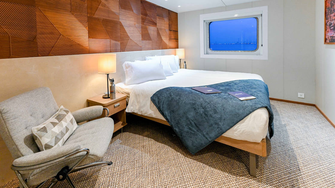 Promenade Deck Stateroom aboard Coral Adventurer small ships with chair, bed, and window.